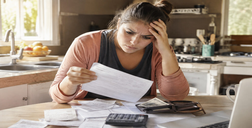 Stressed woman reviewing a credit card bill with receipts, calculator, and wallet at a kitchen table